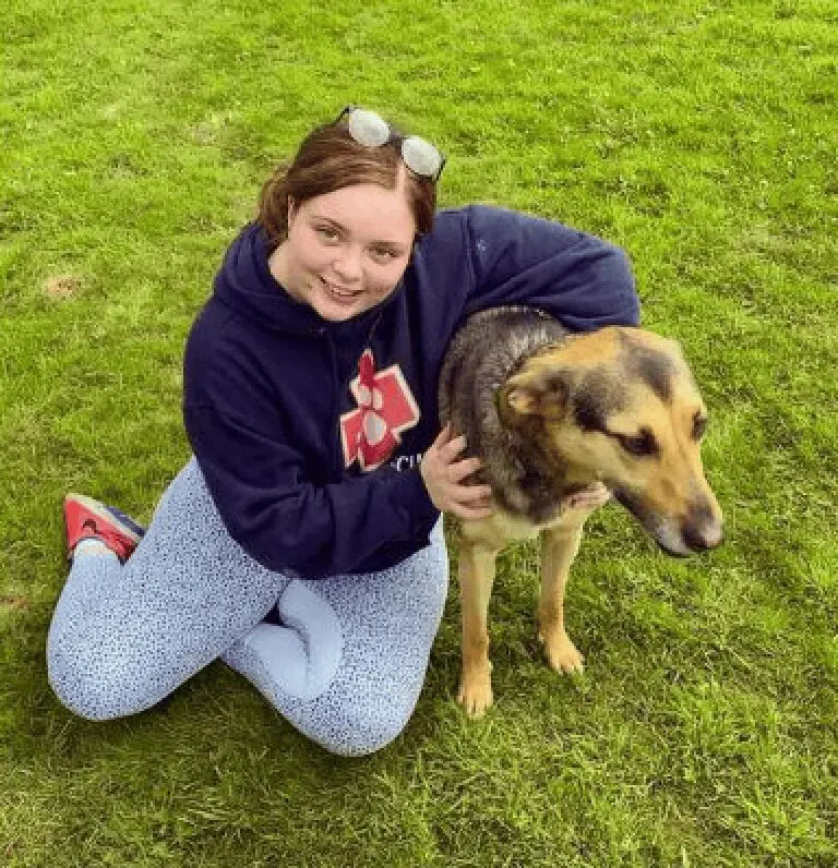 A photo of Paws2Rescue team member Iona sitting on grass outside cuddling a happy dog
